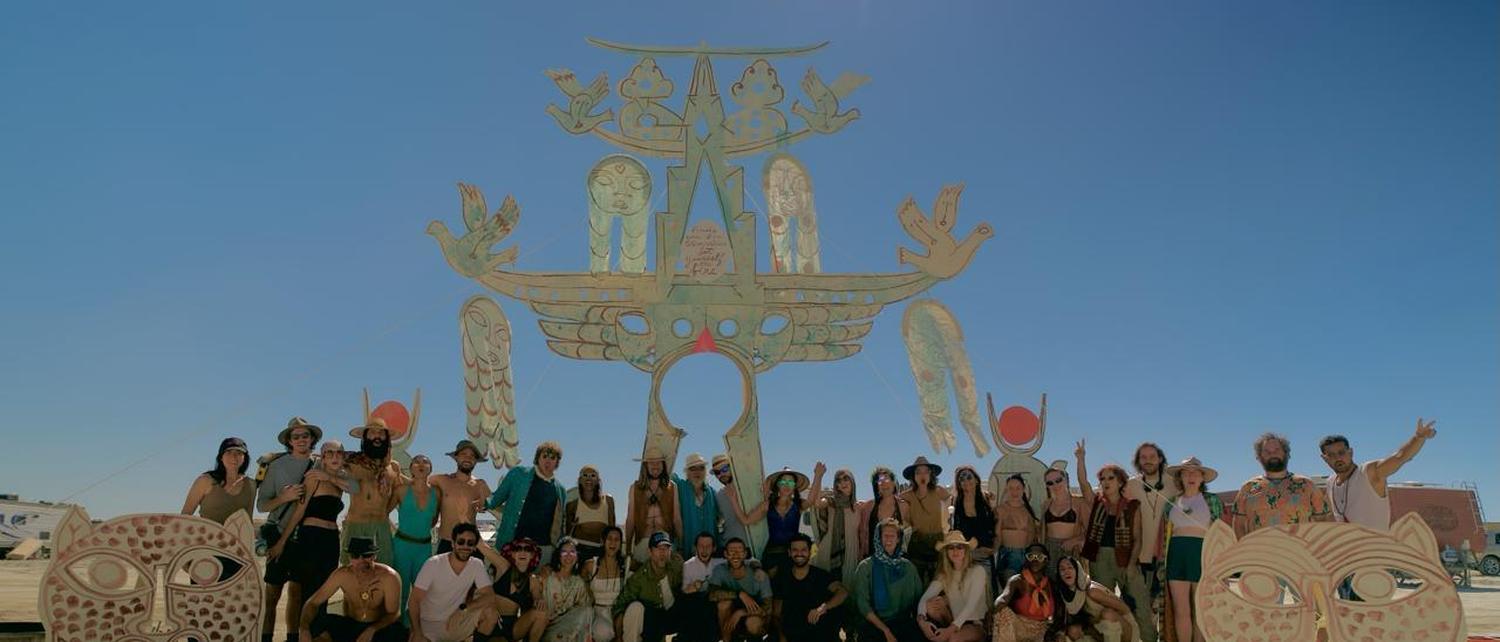 A completed gate standing against an open sky, the whole company gathered beneath it